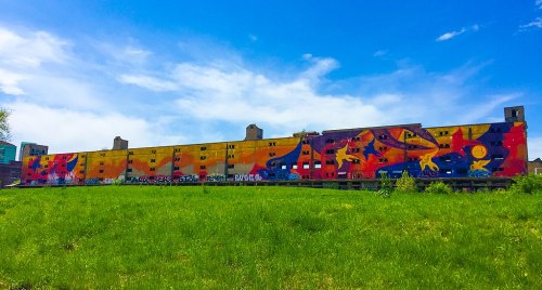 A vibrant mural on a large building, featuring colorful animals and abstract designs against a blue sky.