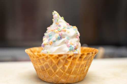 A soft-serve ice cream cone topped with colorful sprinkles in a waffle bowl.