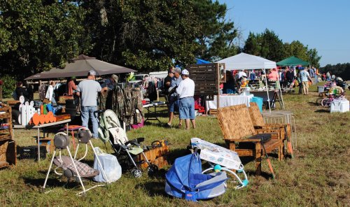 A bustling outdoor market with various stalls, people browsing, and items like strollers and furniture displayed.