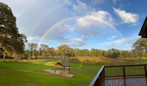 A vibrant rainbow arcs over a green landscape with trees and a gazebo, under a partly cloudy sky.