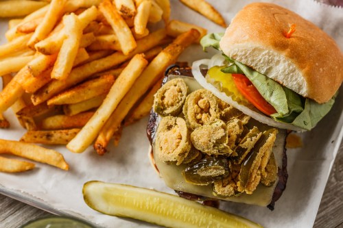A delicious burger topped with pickles, lettuce, tomato, and fried jalapeños, served with crispy French fries.