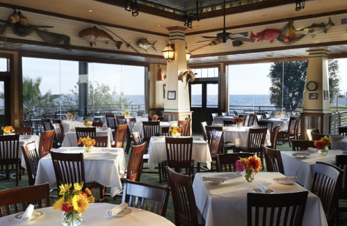 Brightly lit restaurant with tables set for dining, featuring floral centerpieces and a view of the ocean.