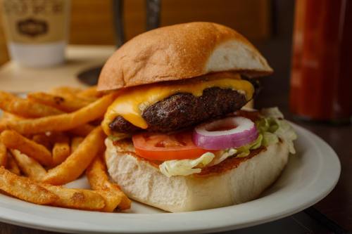 A juicy cheeseburger with lettuce, tomato, and onion, served with crispy fries on a white plate.