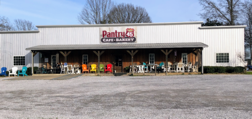 Exterior of Pantry 45 Café-Bakery, featuring a metal building with colorful chairs on the porch and gravel in front.