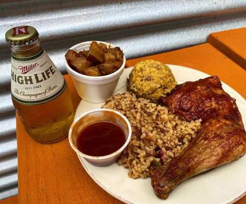 A plate of food with a chicken leg, rice, cornbread, and a side of potatoes, alongside a bottle of Miller High Life beer.
