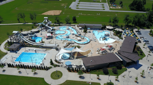 Aerial view of a water park featuring pools, slides, and lounging areas surrounded by green fields and parking.