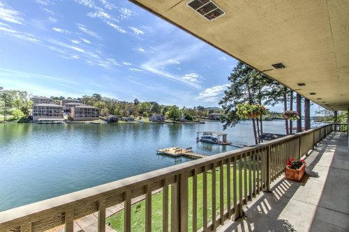 View from a balcony overlooking a serene lake, with boats and lush greenery in the background under a clear blue sky.
