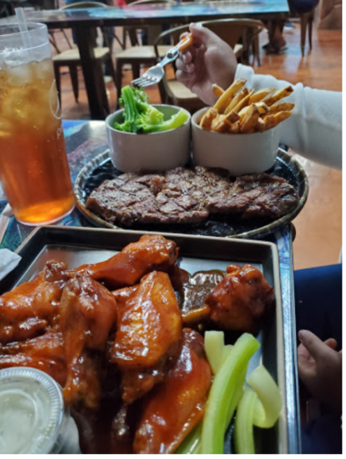 A table with a variety of food: chicken wings, steak, fries, and a salad, alongside a glass of iced tea.