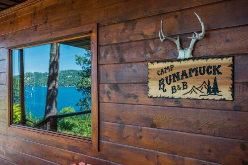 A wooden cabin wall with a sign reading "Camp Runamuck B&B" and a view of a lake and trees through a window.