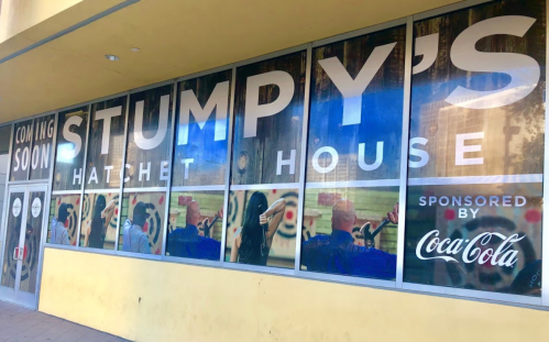 Window display for "Stumpy's Hatchet House," with a "Coming Soon" sign and Coca-Cola sponsorship.