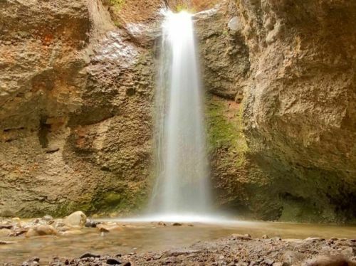 A serene waterfall cascading down rocky cliffs into a clear pool, surrounded by moss and natural stone.