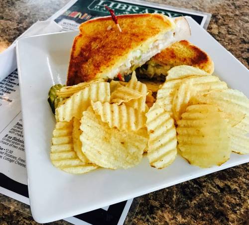 A toasted sandwich with a toothpick, served with a side of ridged potato chips on a white plate.