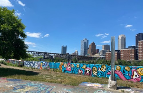 Colorful graffiti murals on a wall with a city skyline and blue sky in the background. Green grass in the foreground.