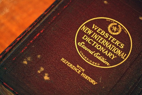 Close-up of a vintage Webster's New International Dictionary, Second Edition, with a worn leather cover and gold lettering.