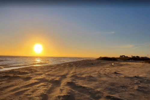 A serene beach at sunset, with golden light reflecting on the water and gentle waves lapping at the sandy shore.