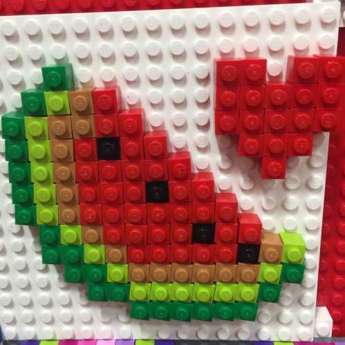 Colorful LEGO mosaic of a watermelon slice with a heart shape above it, set against a white background.