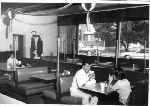 A vintage diner scene with two patrons at a booth, one sipping a drink, and another seated nearby.