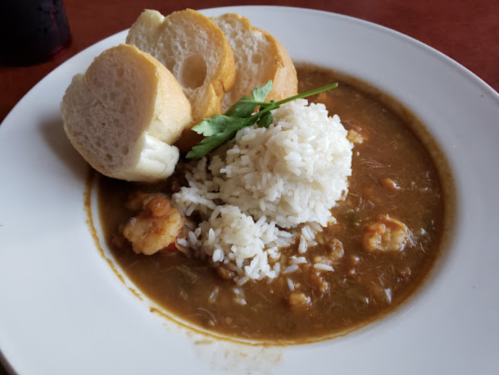 A plate of rice served with shrimp in a brown sauce, accompanied by slices of bread and a sprig of cilantro.