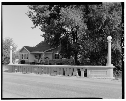 Sign for "Lincoln Highway" in front of a house, surrounded by trees, in a black and white photograph.