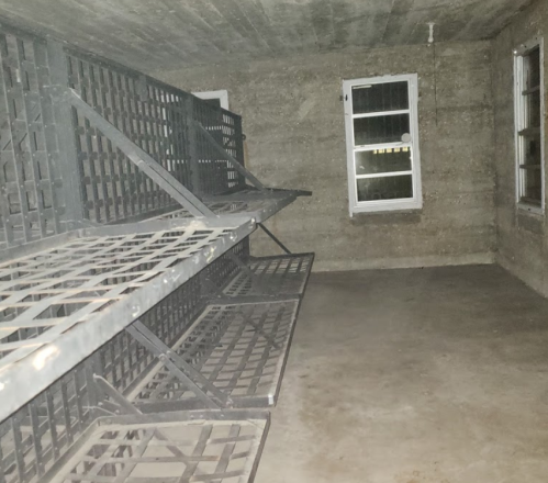 A dimly lit room with metal bunk beds against the walls and a window with bars.