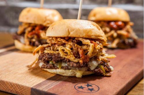 Three delicious sliders topped with crispy onions and sauce, served on a wooden board.