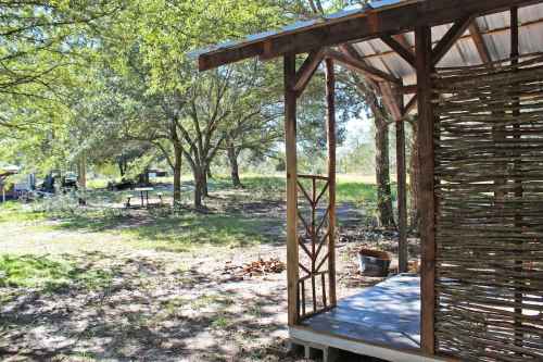 A rustic wooden structure with a porch, surrounded by trees and a grassy area, creating a serene outdoor setting.