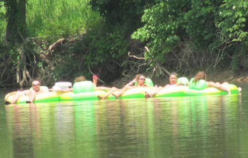 A group of people relaxes on green inflatable rafts in a calm river surrounded by lush greenery.