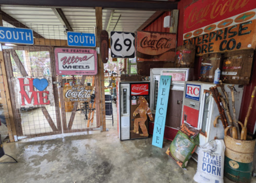A rustic interior featuring vintage Coca-Cola signs, a welcome sign, and old-fashioned vending machines.
