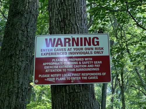 A warning sign on a tree advises entering caves at one's own risk and to notify local first responders.