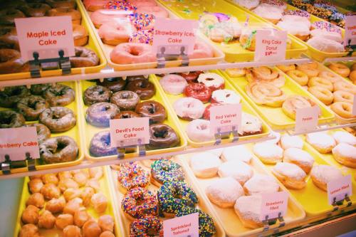 A colorful display of various donuts and cakes, including maple iced, strawberry, and red velvet, in a bakery case.