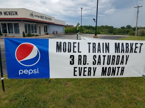 Banner advertising a monthly model train market, sponsored by Pepsi, outside a museum.