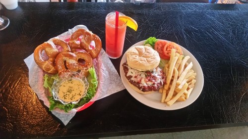 A plate with a burger, fries, and a side of lettuce, tomato, alongside a basket of pretzels and a drink.