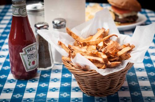 A basket of golden fries on a blue checkered tablecloth, with ketchup and condiments in the background.
