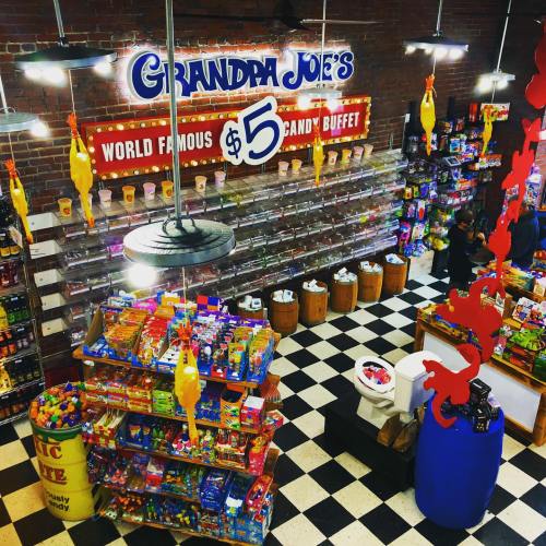 A colorful candy store with shelves of sweets, a buffet sign, and playful decor, including rubber chickens hanging from the ceiling.