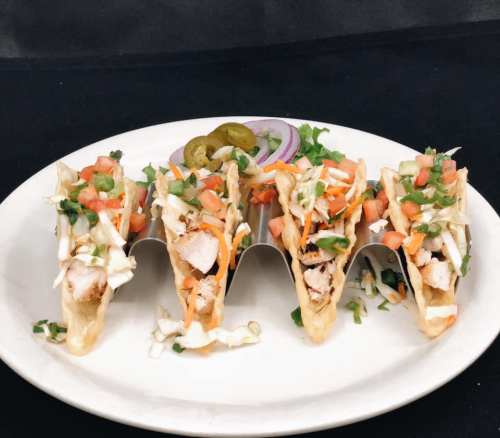 Five tacos filled with chicken, lettuce, tomatoes, and topped with jalapeños, served on a white plate.
