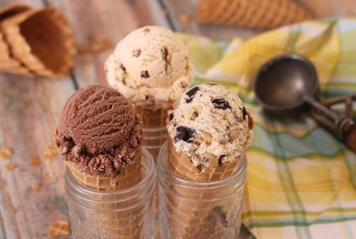 Three ice cream cones in jars: chocolate, cookie dough, and vanilla with chocolate chips, on a wooden table with a checkered cloth.