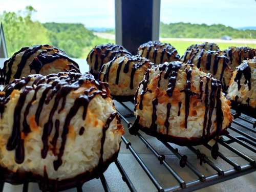Freshly baked coconut macaroons drizzled with chocolate, cooling on a wire rack with a scenic background.
