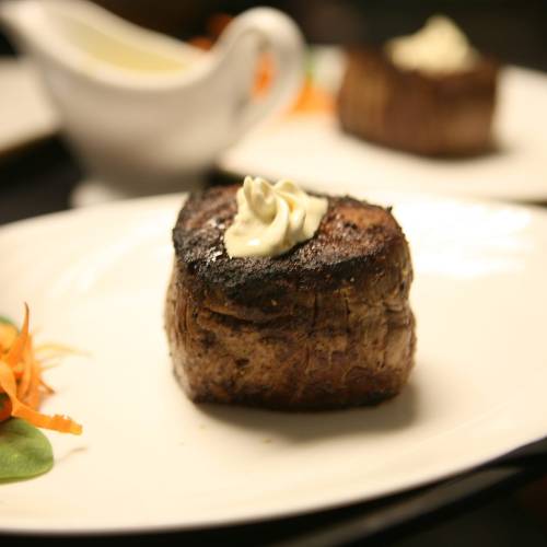 A perfectly cooked steak topped with a dollop of butter, served on a white plate with garnishes.