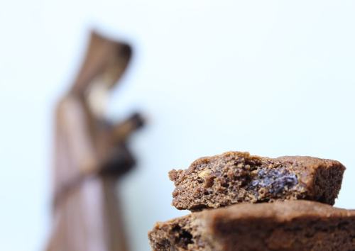 Close-up of chocolate brownies in the foreground with a blurred wooden figure in the background.
