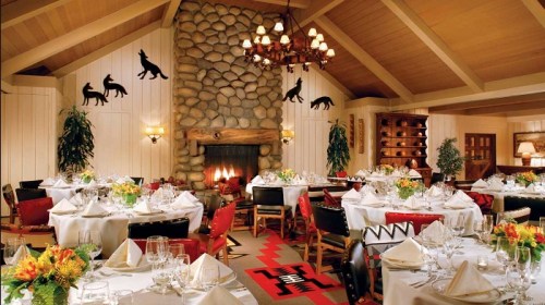 Cozy dining room with stone fireplace, elegant tables, and Native American-inspired decor. Warm, inviting atmosphere.