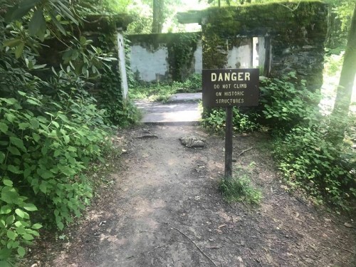 A path leads to a moss-covered stone structure with a "Danger" sign warning against climbing on historic structures.