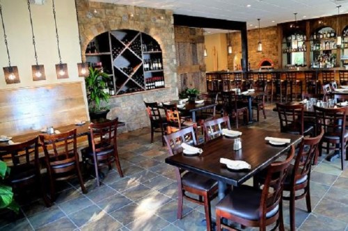 Cozy restaurant interior with wooden tables, chairs, and a wine rack, featuring warm lighting and stone accents.