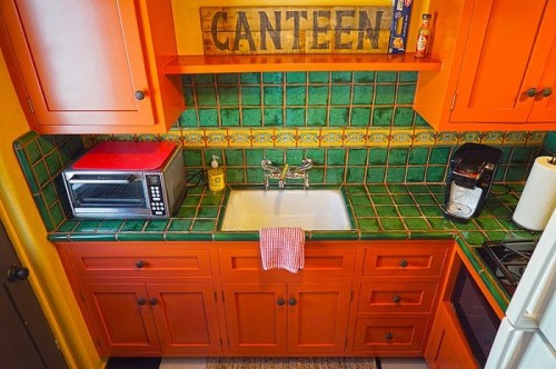 Colorful kitchen with orange cabinets, green tiled backsplash, a sink, microwave, and coffee maker on the counter.