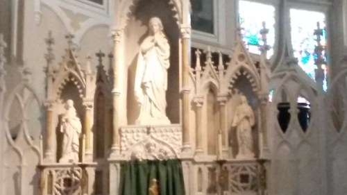 A decorative altar with a central statue of a figure, flanked by two smaller statues, set in a church interior.