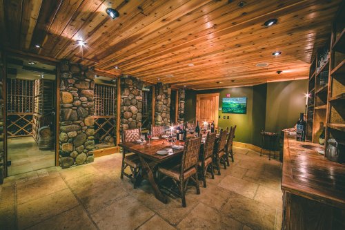 Cozy dining room with a wooden ceiling, stone walls, a large table set for dinner, and soft lighting.
