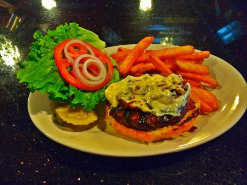 A plate with a burger topped with cheese, lettuce, tomato, onion, pickles, and a side of crispy fries.