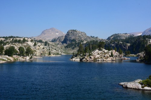 A serene lake surrounded by rocky hills and trees under a clear blue sky.
