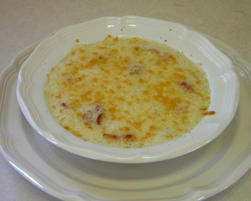 A creamy, baked dish with a golden, cheesy top served in a white dish on a light-colored surface.