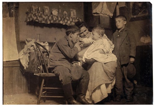 A sepia-toned photo of a woman with three children, two boys and a baby, in a rustic interior setting.