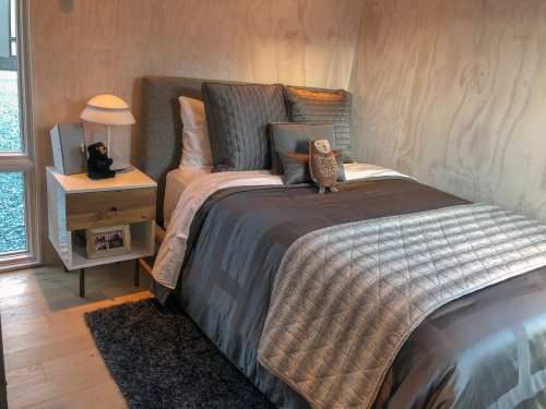 Cozy bedroom with a bed, decorative pillows, a nightstand, and a lamp, featuring warm wood paneling and soft lighting.
